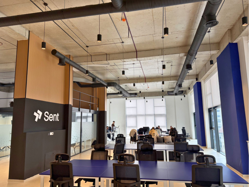 The Sent team at a long table in the Kosovo office, under the wordmark on the back wall